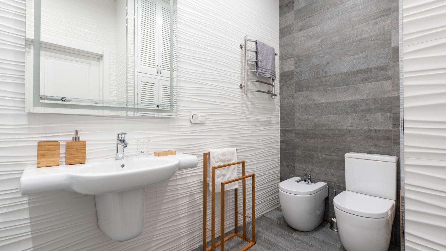 Modern pristine bathroom with white textured tiles, pedestal sink, glass shower, and wood accents - perfect move-in ready condition