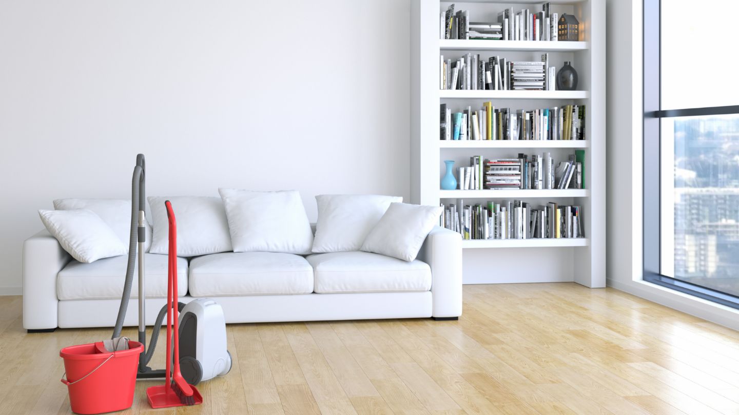 Modern minimalist living room with white sectional sofa, built-in bookshelf, and spotless hardwood floors with professional cleaning supplies visible