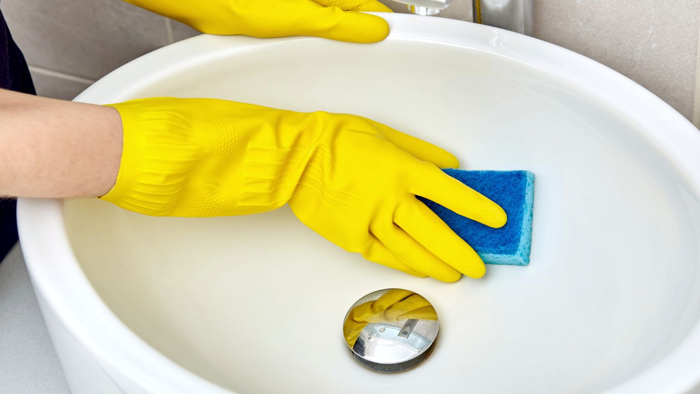 Professional office bathroom cleaning with person in yellow gloves scrubbing white bathtub with blue cleaning sponge