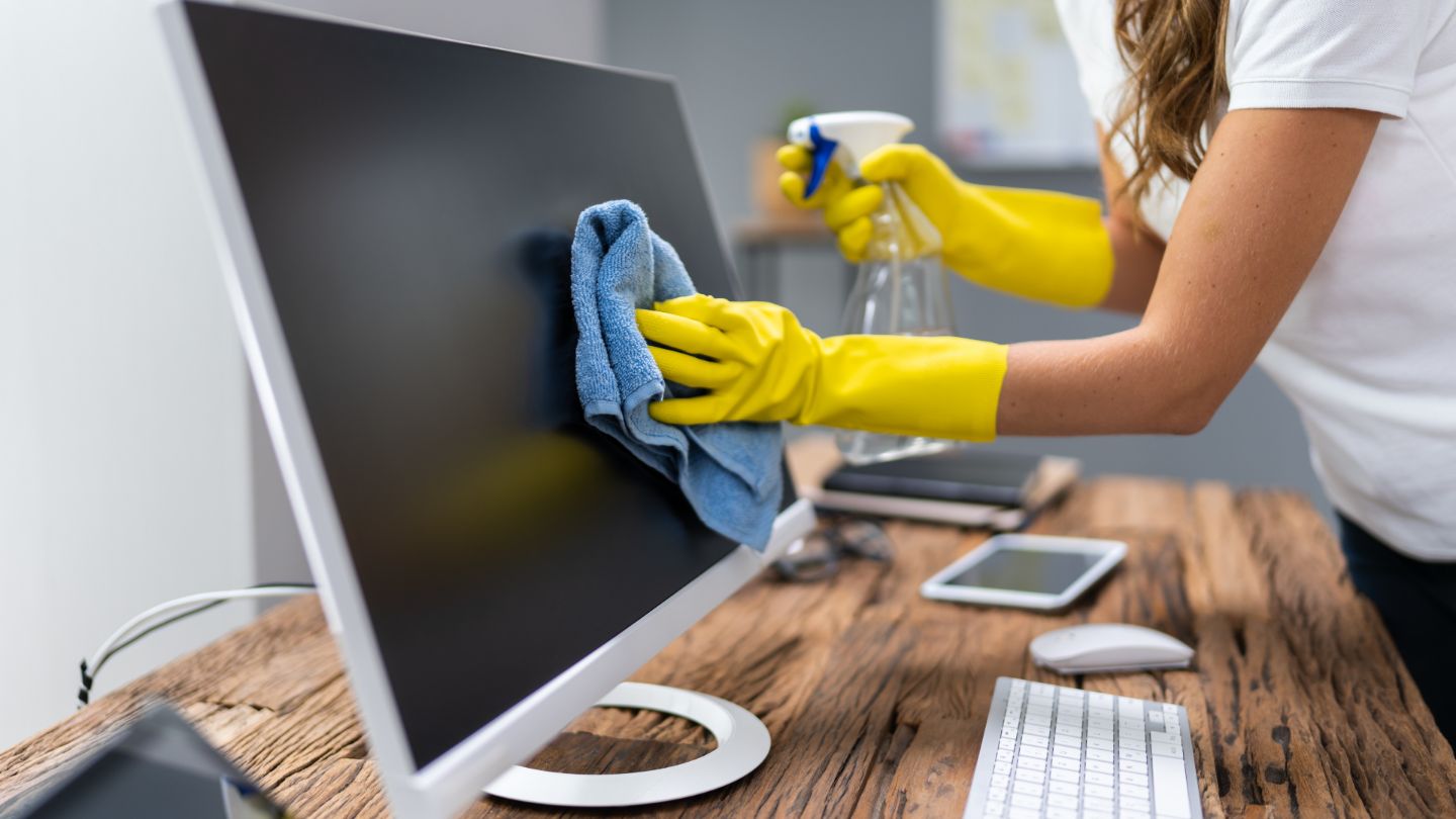 Professional office cleaning with person in yellow gloves sanitizing computer monitor and workspace