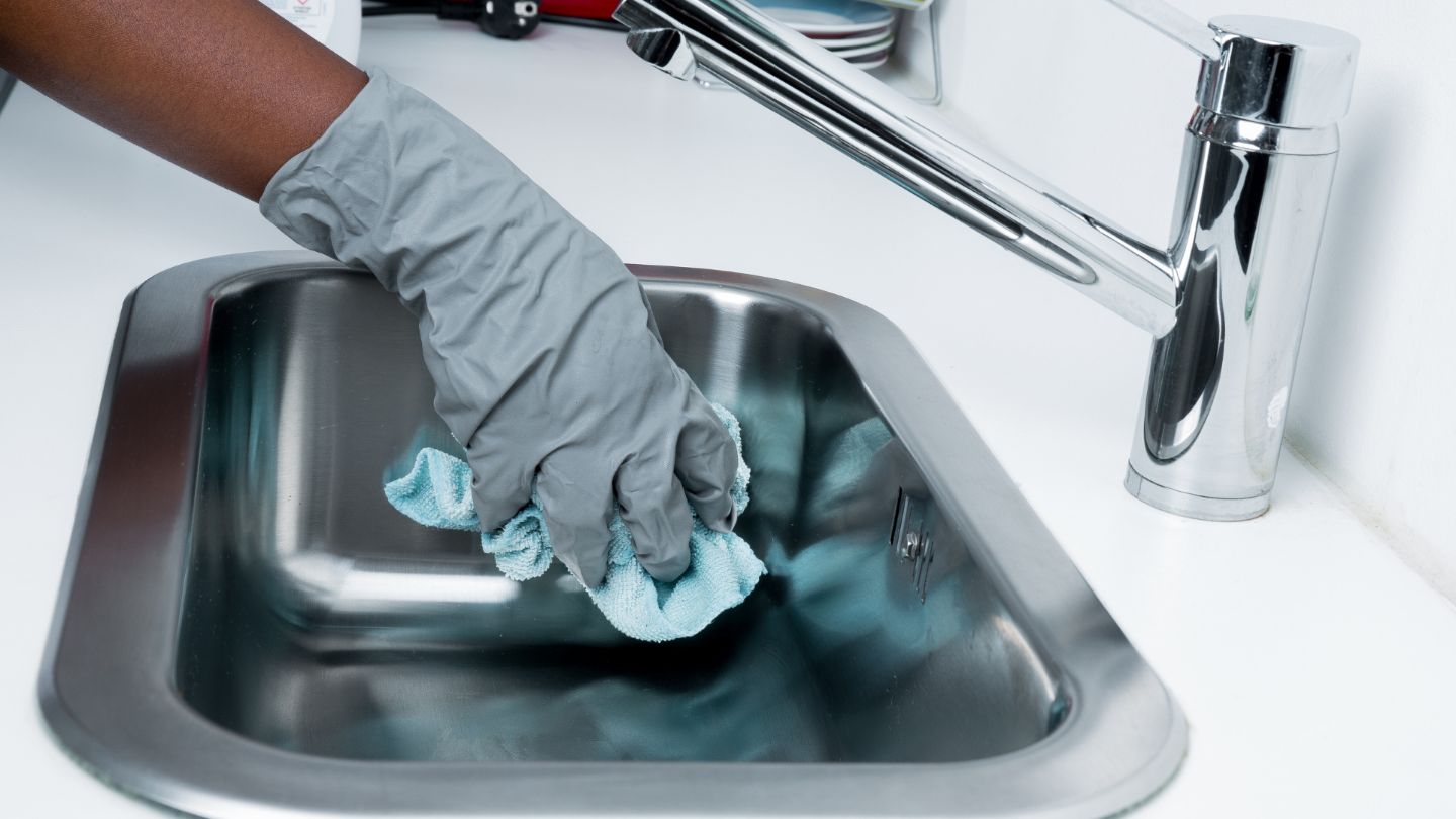 Professional office kitchen cleaning with person in gray gloves sanitizing stainless steel sink with microfiber cloth