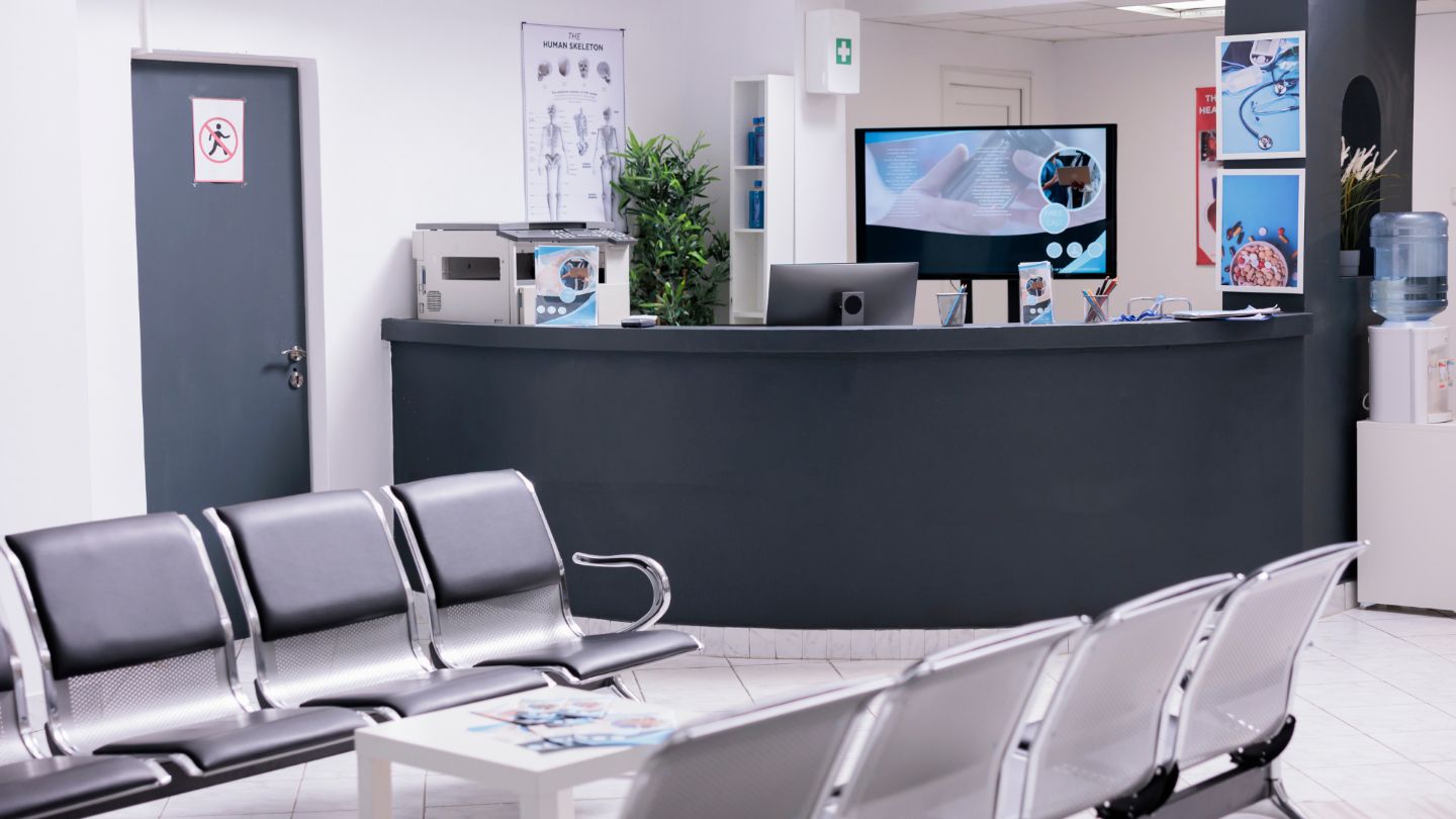 Professional medical office reception area with dark reception desk, computer equipment, and modern gray waiting chairs